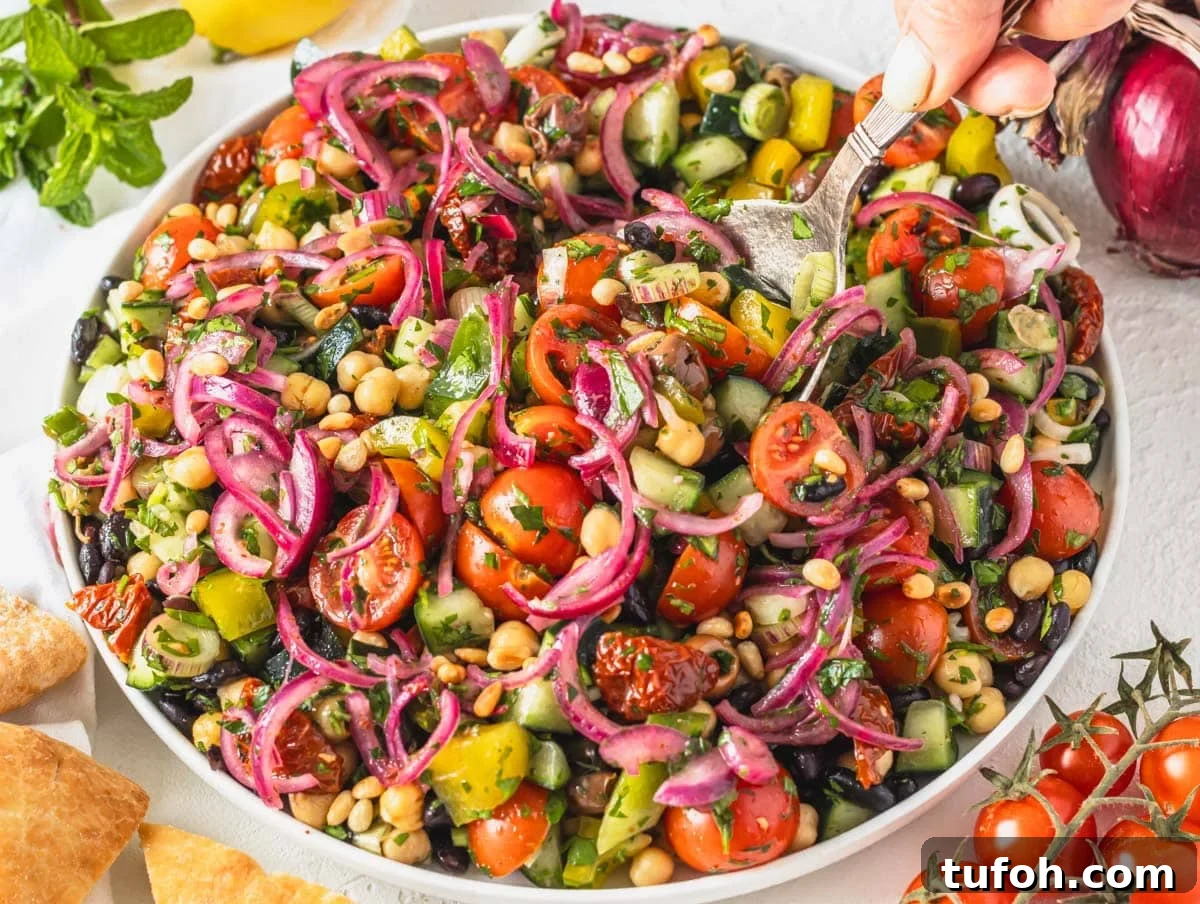 Balela salad with sumac onions on a white plate with hand holding a spoon
