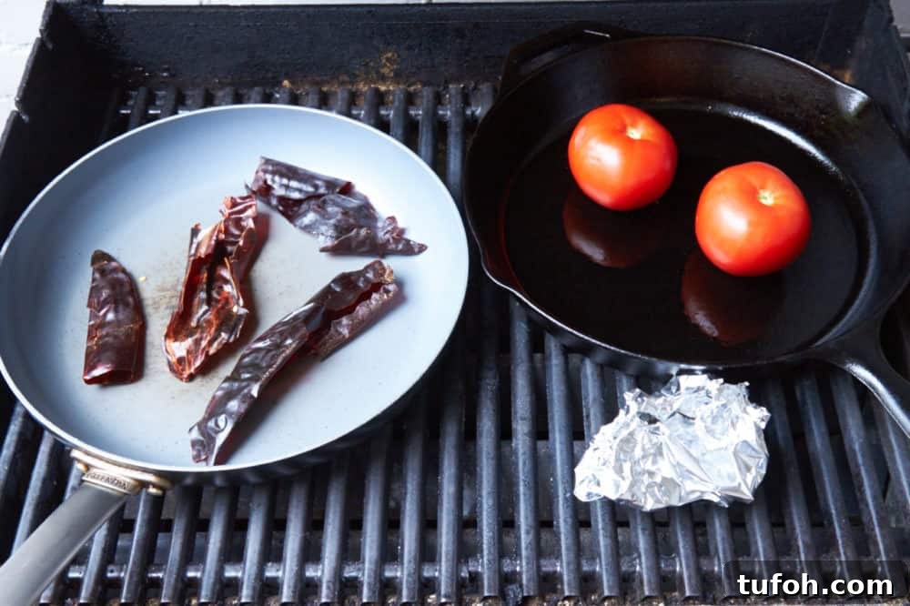Orange-Almond Mole Sauce: Quick Recipe for Vibrant Flavor 5 A grill with two skillets, one containing dried chiles, the other containing tomatoes. A foil pouch with roasting garlic sits beside them.