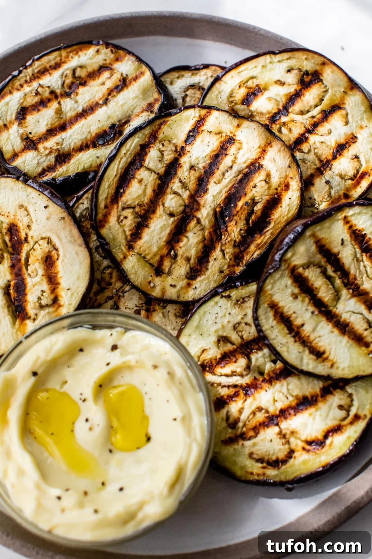grilled eggplant rounds on a plate with garlic aioli on the side