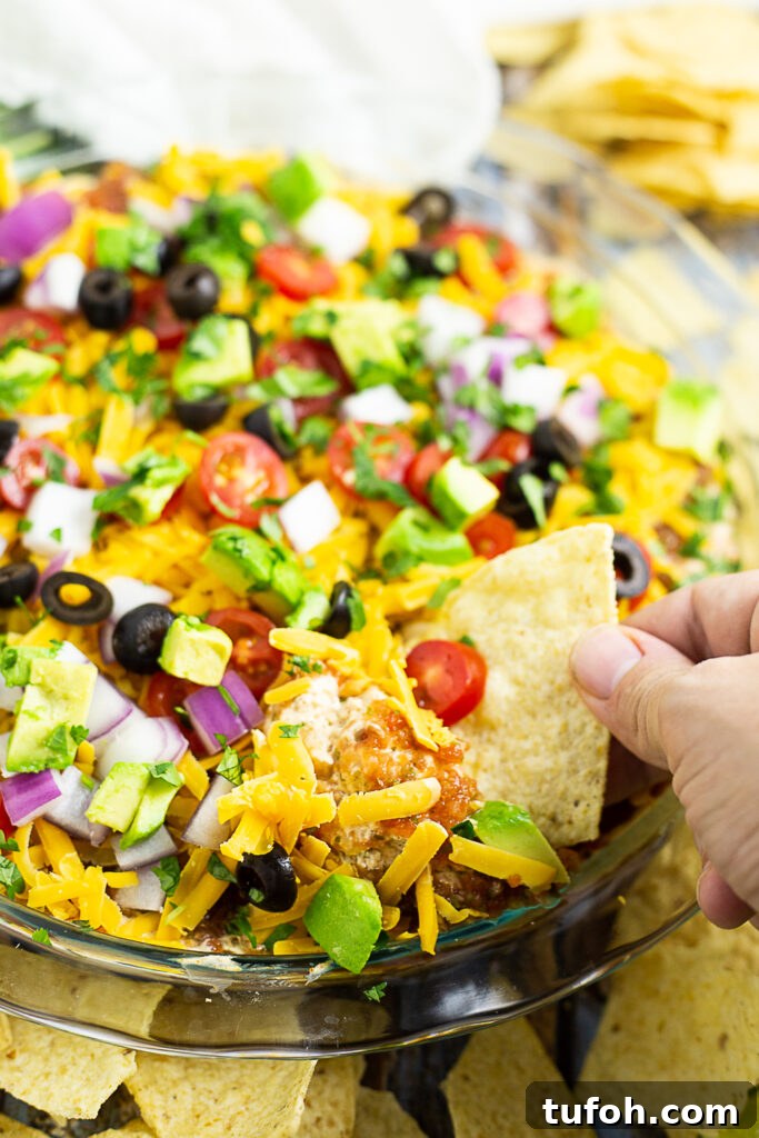 Easy layered taco dip in a round glass dish with a tortilla chip dipping into it