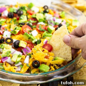Easy layered taco dip in a round glass dish with a tortilla chip dipping into it