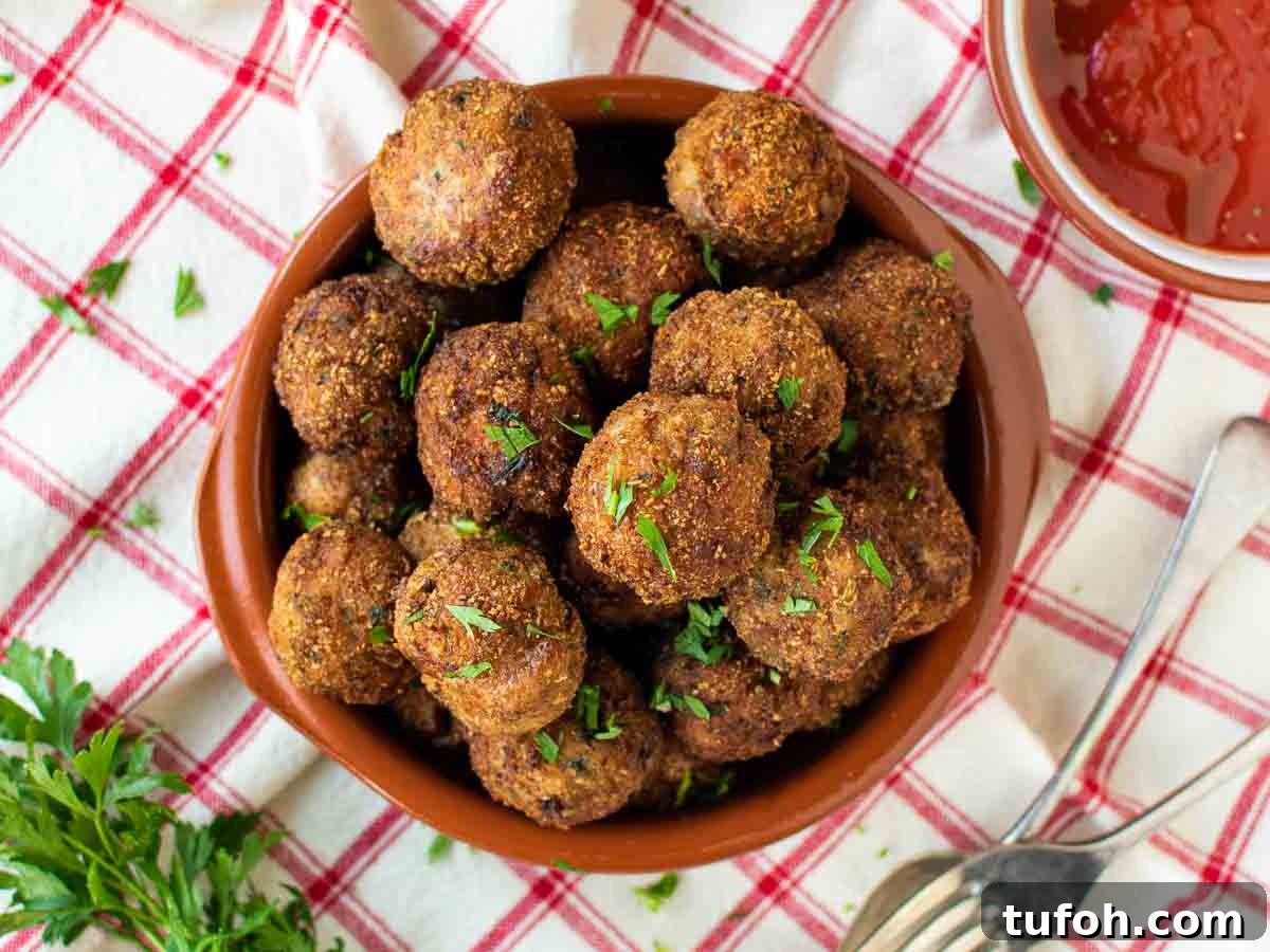 Brown meat balls piled onto a plate on a red and white checked tablecloth.