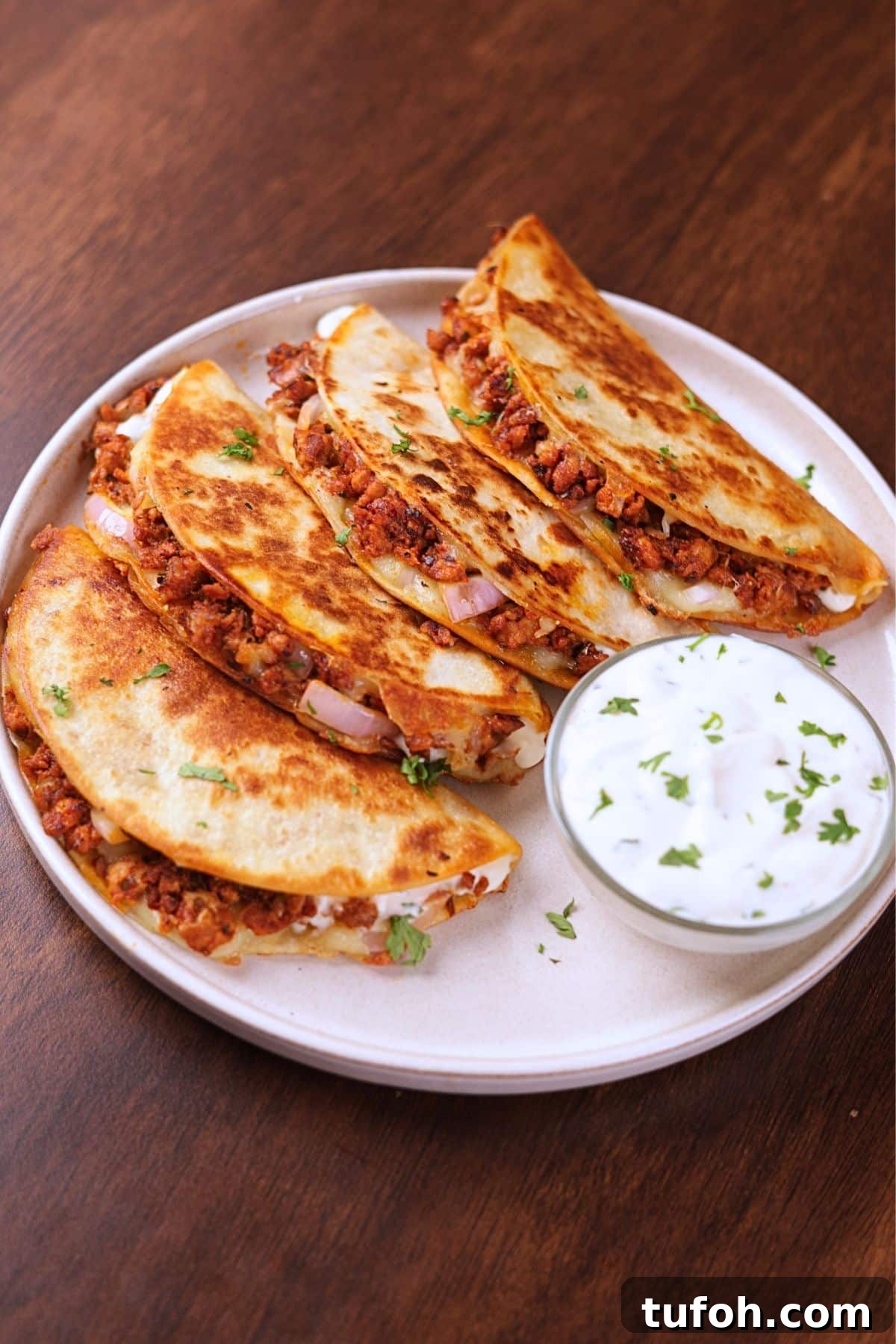Crispy ground chicken tacos served on a white plate with creamy sauce on the side.