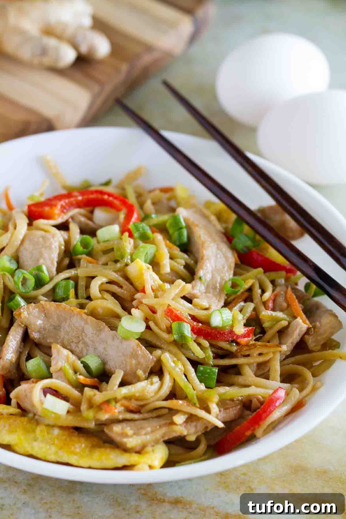 shallow bowl with egg and pork lo mein with chopsticks