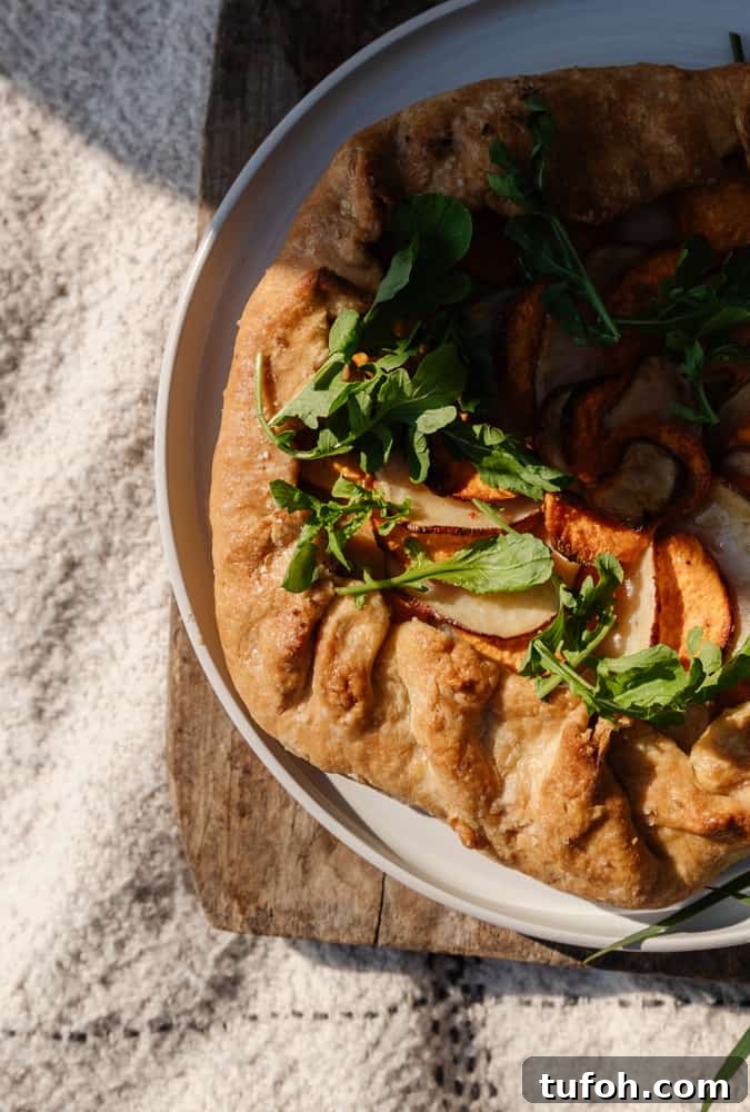 rustic potato galette with fresh arugula on top on a white plate sitting on a rustic wood board on top of a white blanket