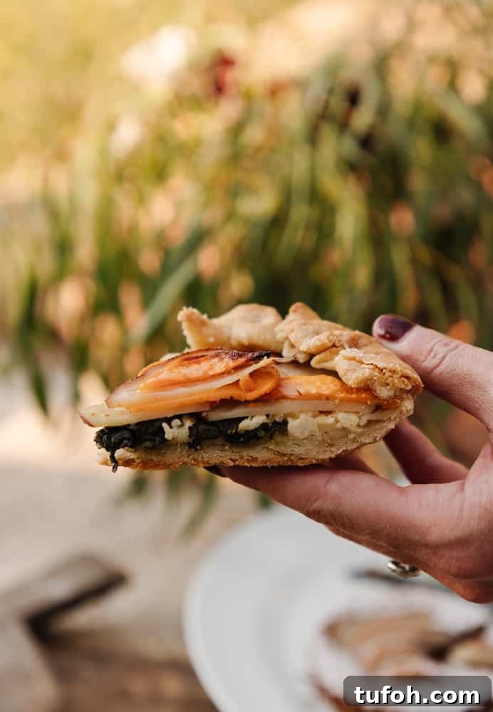 womans hand holding a slice of potato and kale galette with out of focus background
