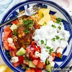 Closeup of overhead of a blue bowl of Greek chicken and rice with tomato, cucumber and feta salad and tsatziki.
