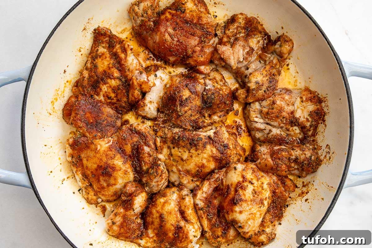 Overhead view of seasoned Greek chicken thighs covered in seasoning and browned in a wide cast iron pan.