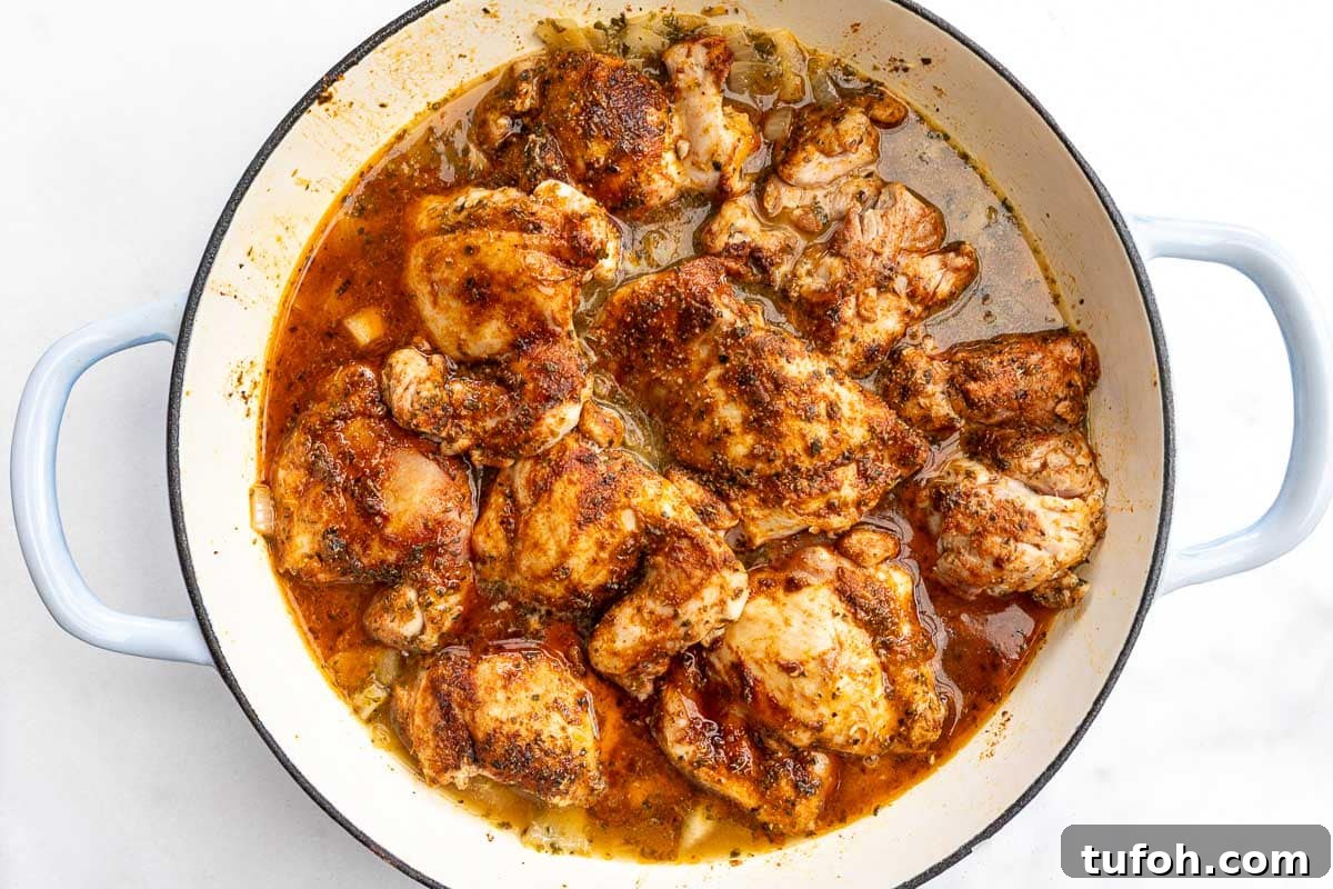 Overhead view of a pan of browned chicken thighs on top of rice and broth.