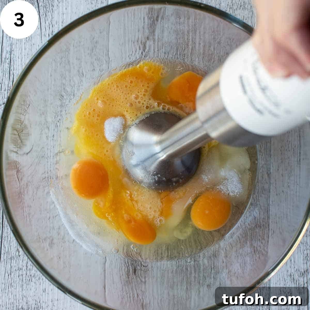 Eggs and sugar being whisked with an emersion blender.