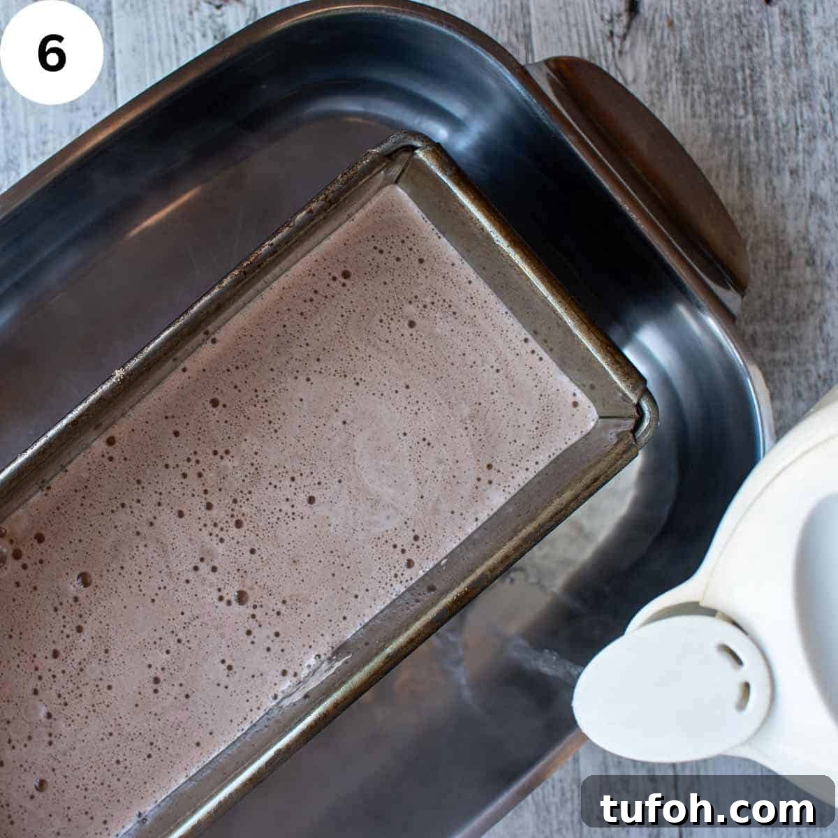 Light brown creamy liquid in a loaf pan in a large baking pan with water being poured in.