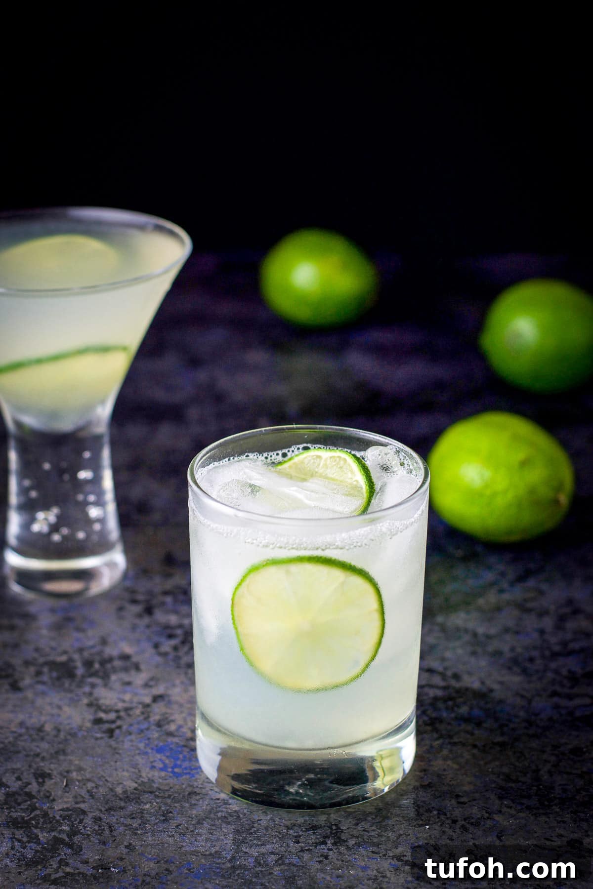 Two lime wheels floating in the gimlet with limes on the table