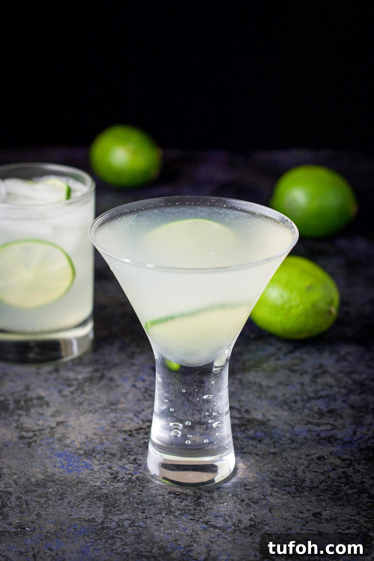 The martini glass filled with the lime drink with garnish and limes in the back