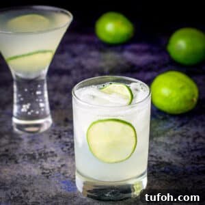 Two glasses filled with the vodka gimlet with whole limes in the background - square