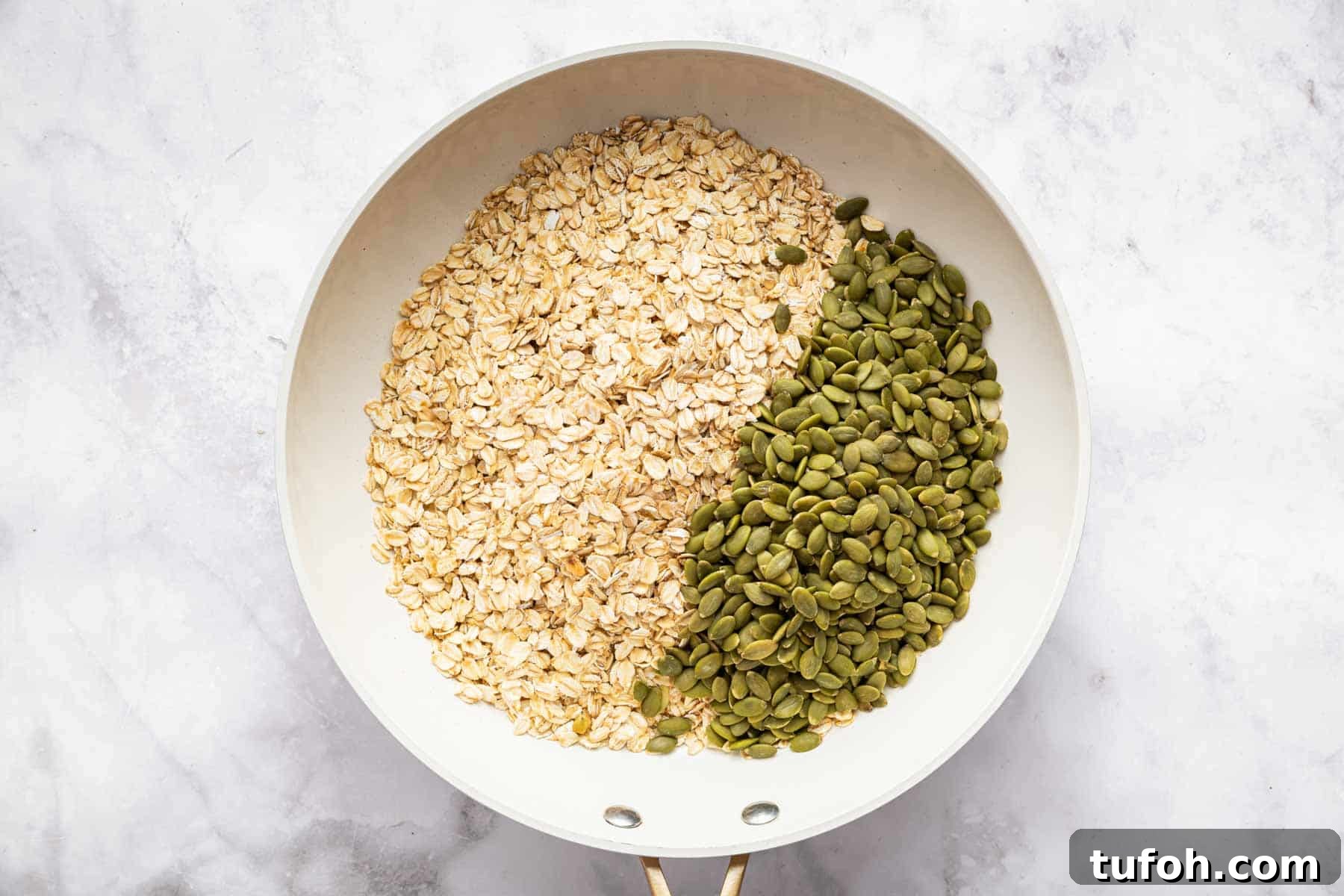 Rolled oats and pumpkin seeds in a white skillet.