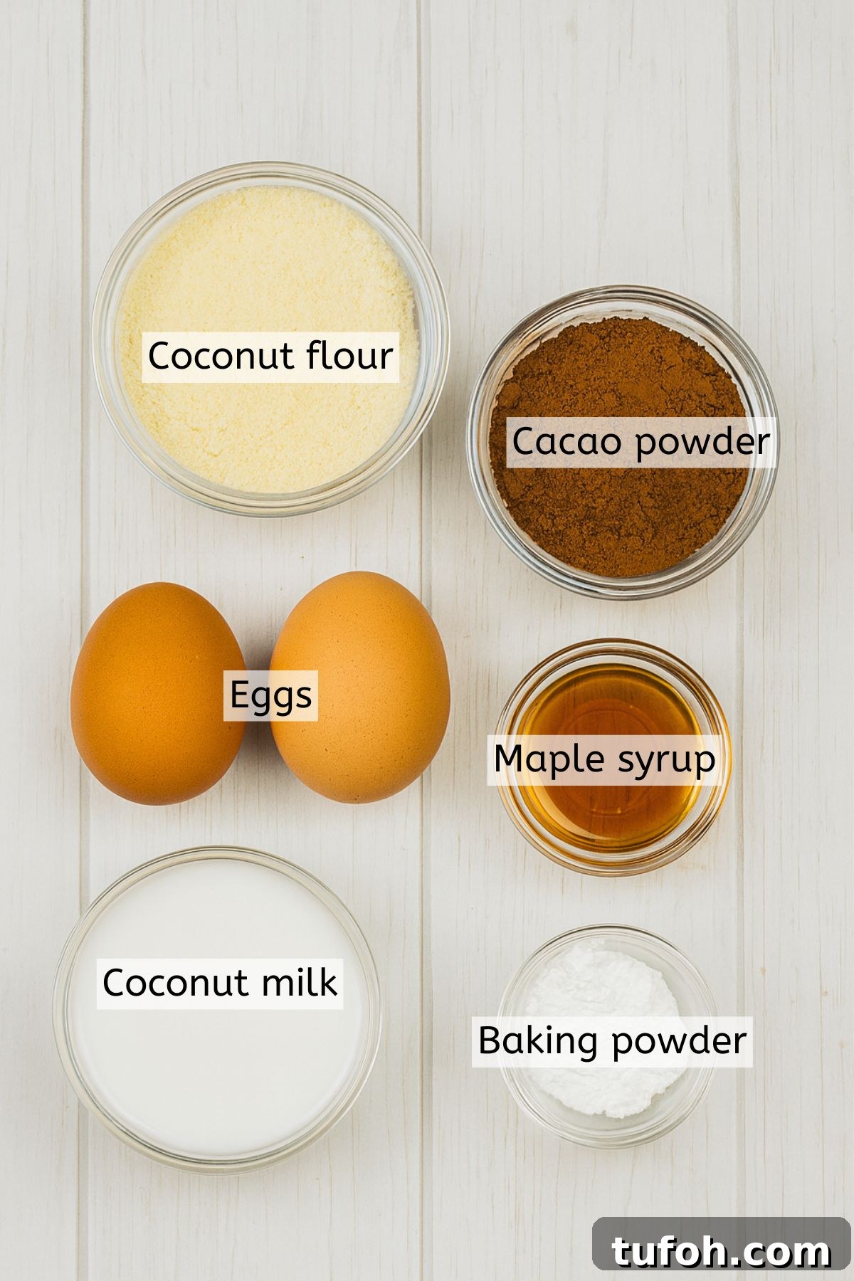 Coconut flour. cacao, maple syrup, and milk in bowls with eggs beside them and text labels over everything.
