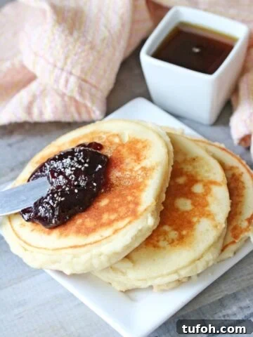 Three yogurt pancakes on a white plate topped with jam.