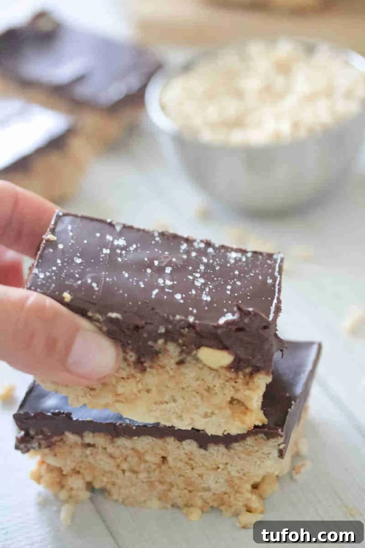 Two fingers placing a chocolate topped protein rice krispie treat on top of another one.