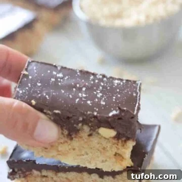 Two fingers placing a chocolate topped protein rice krispie treat on top of another one.