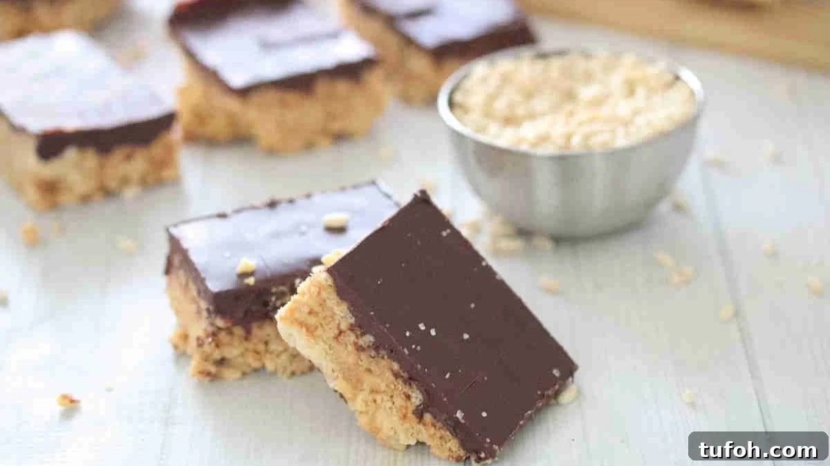 Two squares of protein rice krispies topped with chocolate leaning on each other and more in the background.