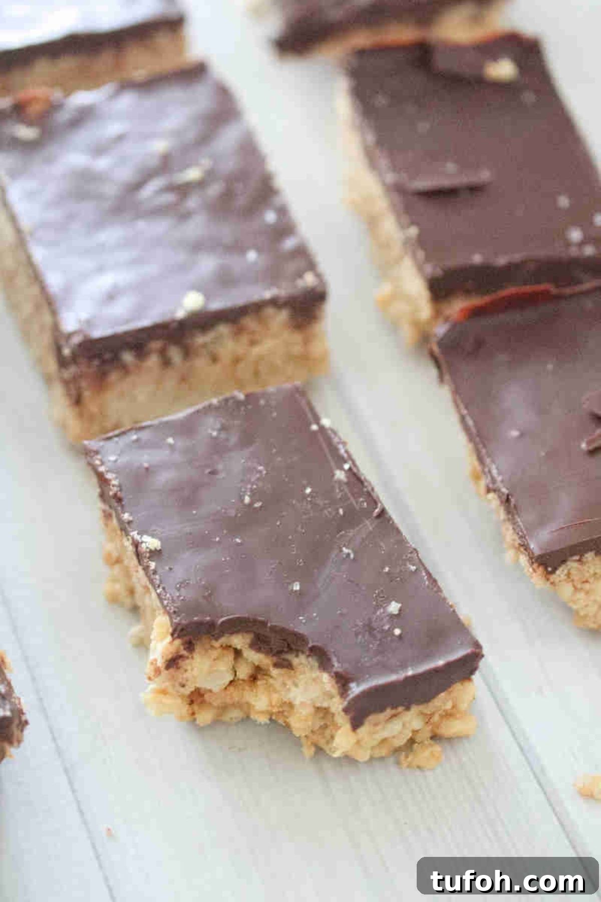 Multiple chocolate topped protein rice krispie squares lined up with a bite out of the front one.