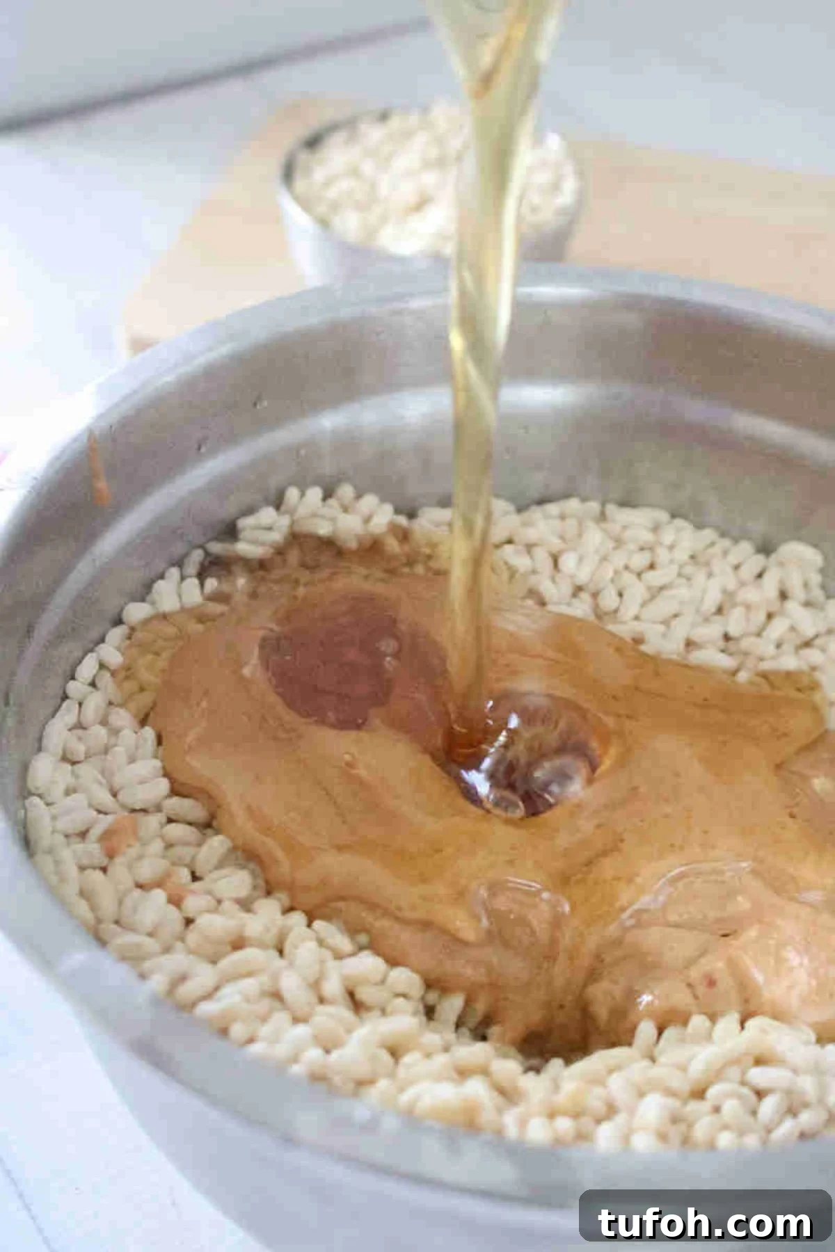 Maple syrup being poured into a bowl with crispy rice and peanut butter.
