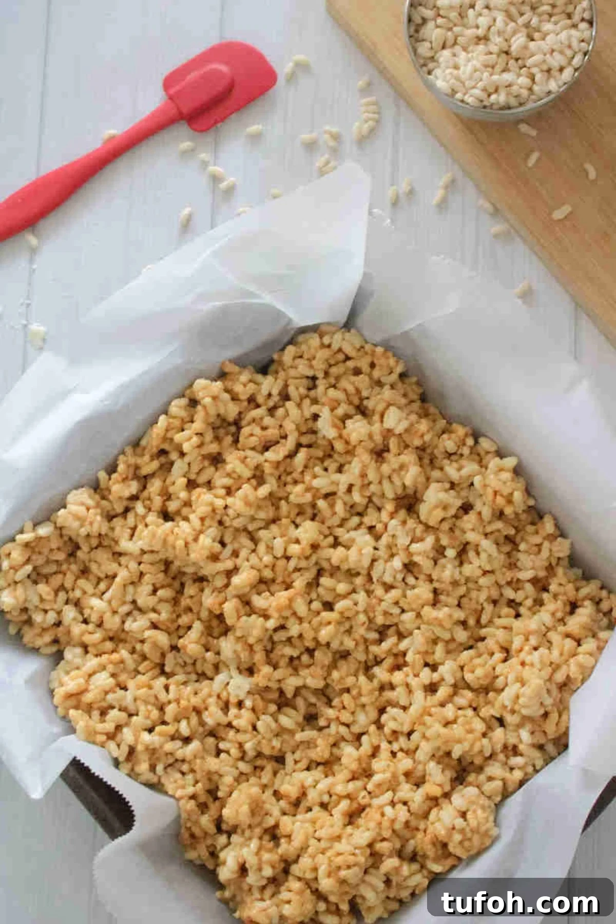 Peanut butter protein rice krispie mix in a parchment paper lined baking pan.