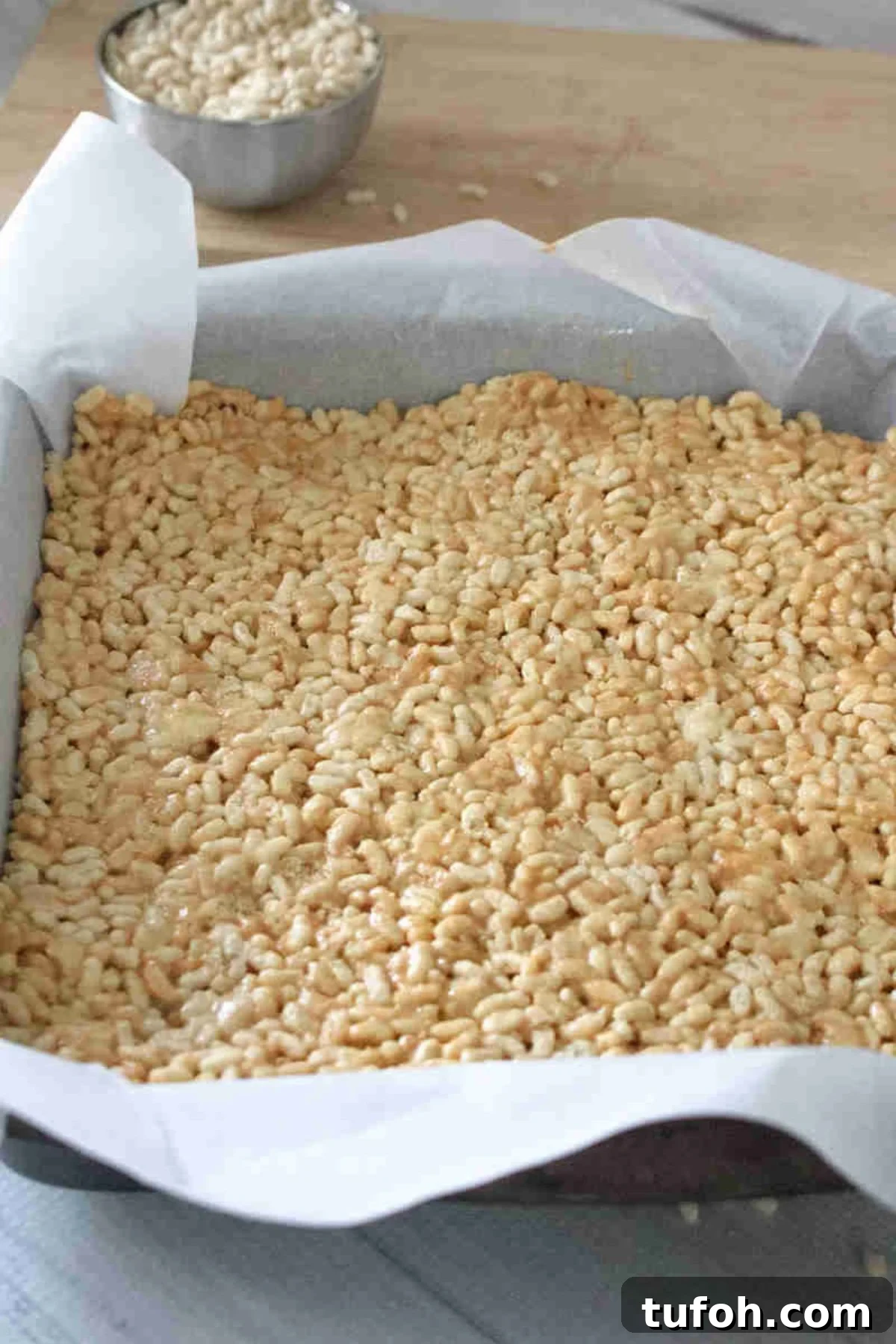 Peanut butter protein rice krispie mix pressed into a pan with parchment paper.