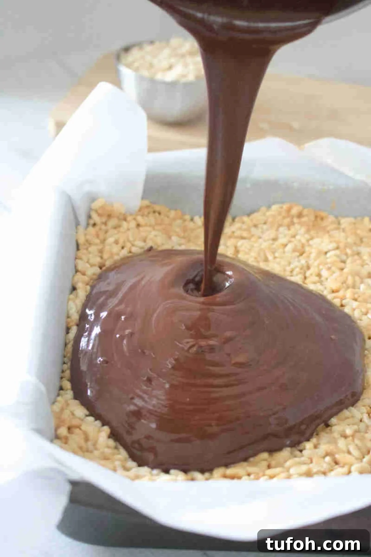 Chocolate sauce being poured on peanut butter protein rice krispie squares.