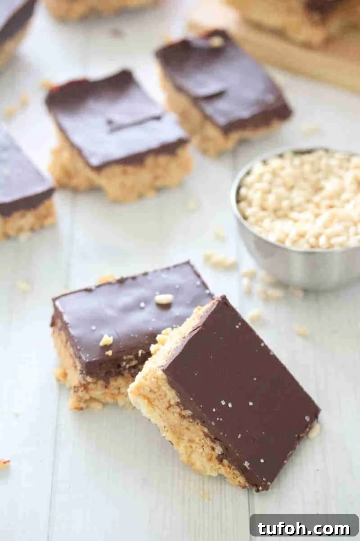 Two squares of protein rice krispies topped with chocolate leaning on each other and more in the backgorund.